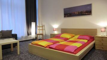 Ein ordentlich eingerichtetes Schlafzimmer mit Bett, Nachttischen, einem Sessel, einem Schreibtisch und einem Fenster mit Vorhängen.
