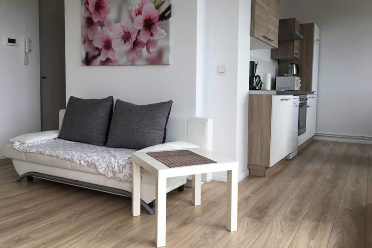A modern living room with a sofa, a small table, and a kitchen area with wooden cabinets and appliances.