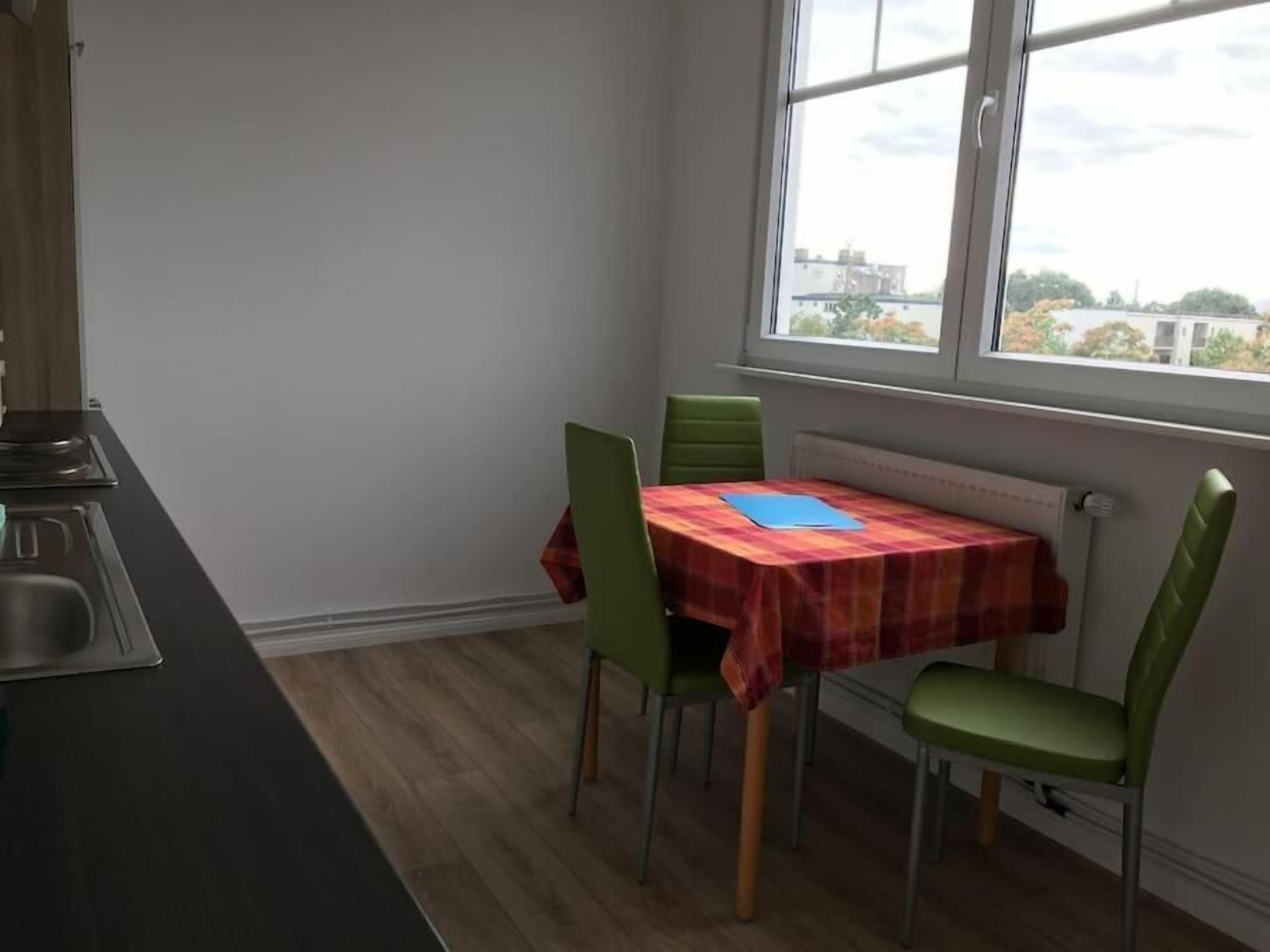 A small kitchen with a dining table and chairs, a window with a view of buildings, and a radiator under the table.