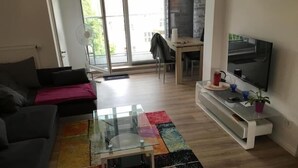 Ein modernes Wohnzimmer mit einer Couch, einem Glastisch, einem Fernseher und einem farbenfrohen Teppich.