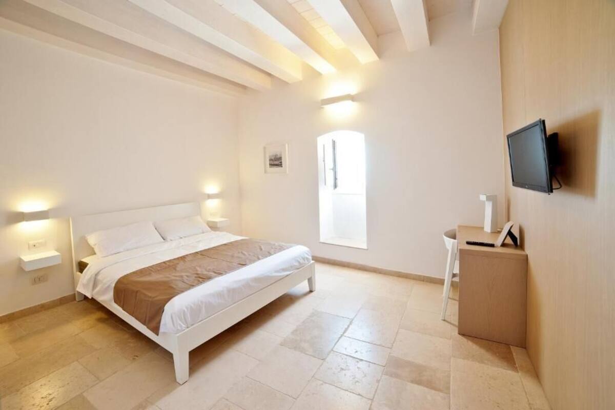 Un dormitorio con cama, mesitas de noche, televisor y ventana.