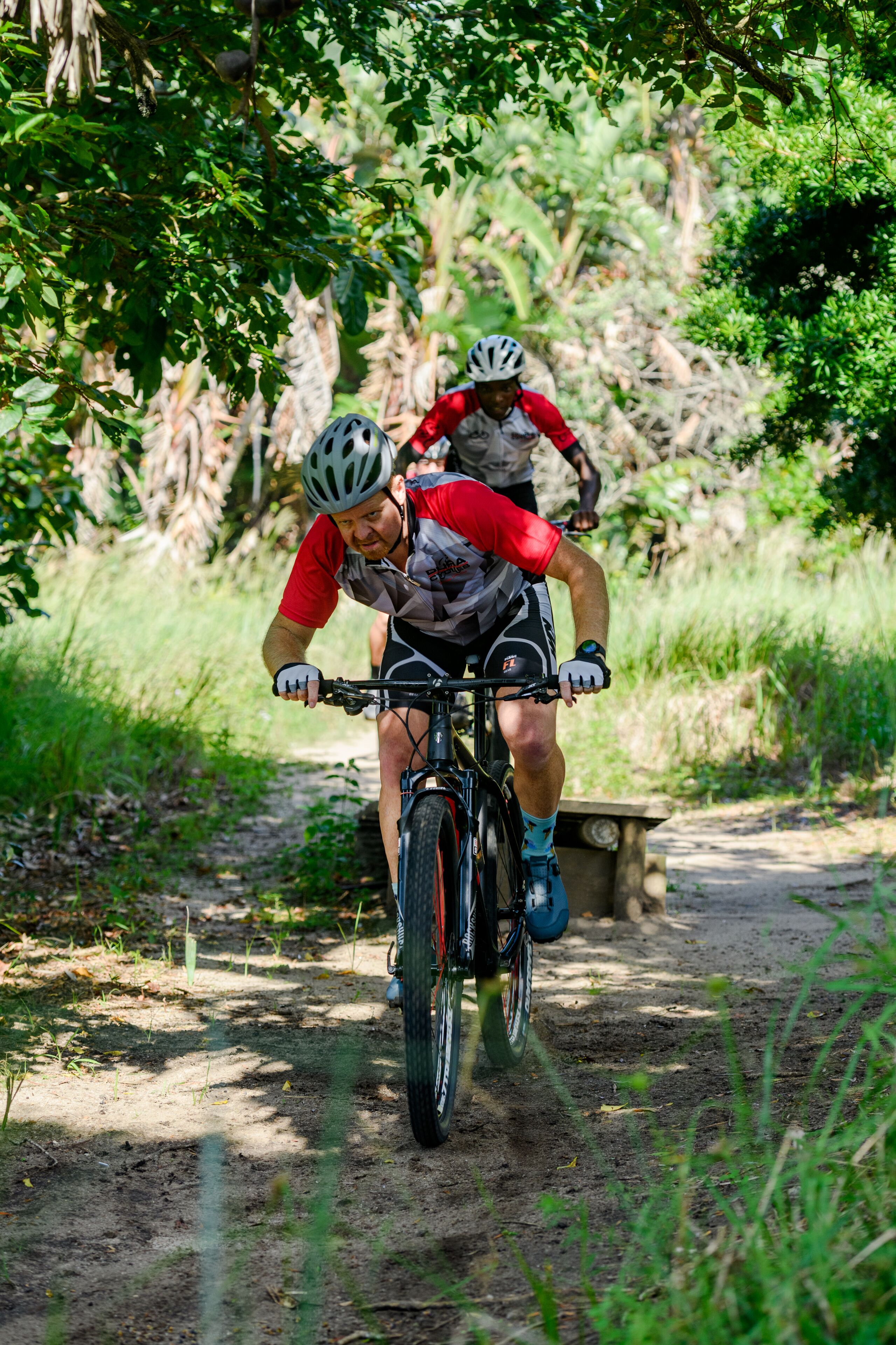Two cyclists on a dirt path surrounded by greenery.