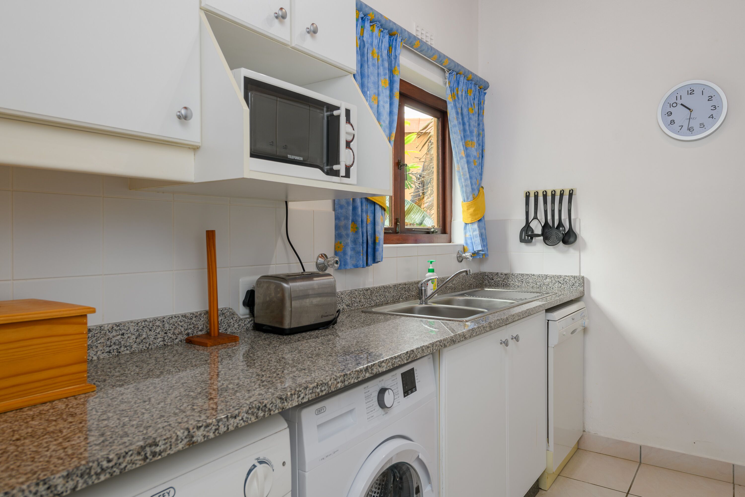 A compact kitchen with a microwave, toaster, sink, and washing machine.
