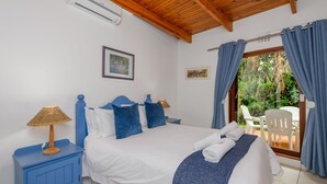 A bedroom with a bed, a nightstand, a window with curtains, and a view of an outdoor patio. - San Lameer Villa Rentals  2843 (Southbroom)