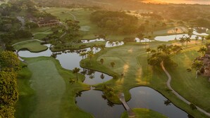A golf course with water hazards, palm trees, and a clubhouse. - San Lameer Villa Rentals  2843 (Southbroom)