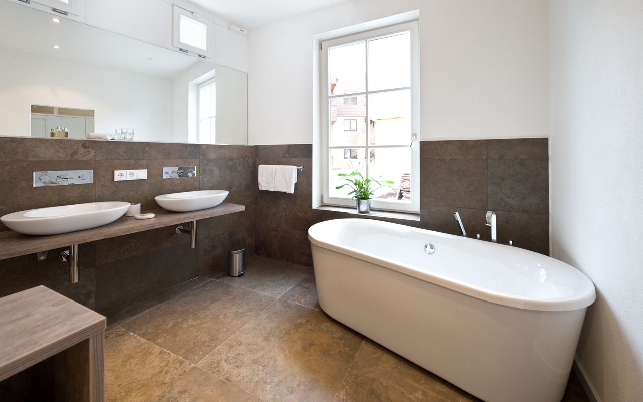 Un baño moderno con una bañera independiente, dos lavamanos y un ventanal que proporciona luz natural.
