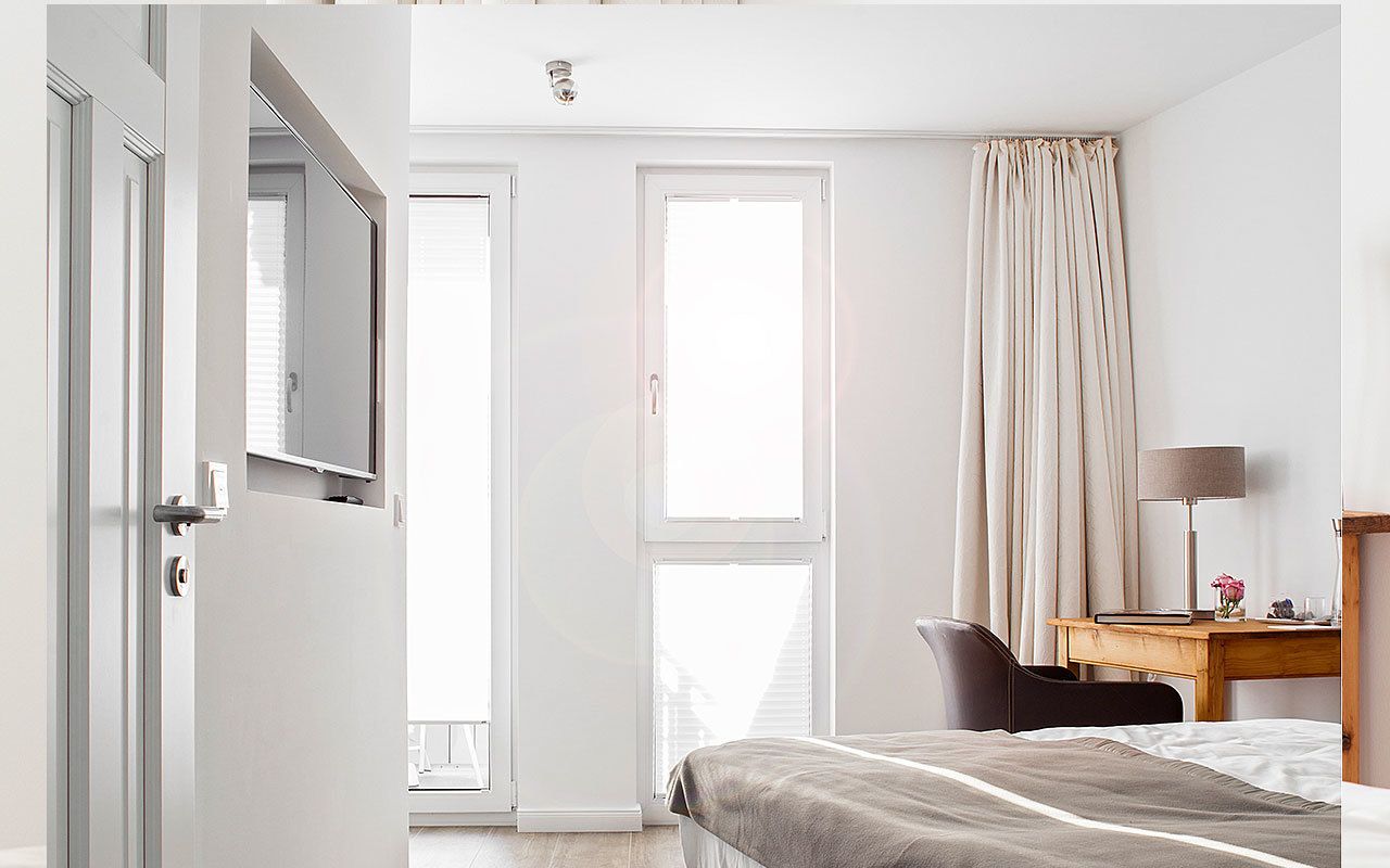 A hotel room with a bed, a desk with a lamp, a chair, and a window with curtains.