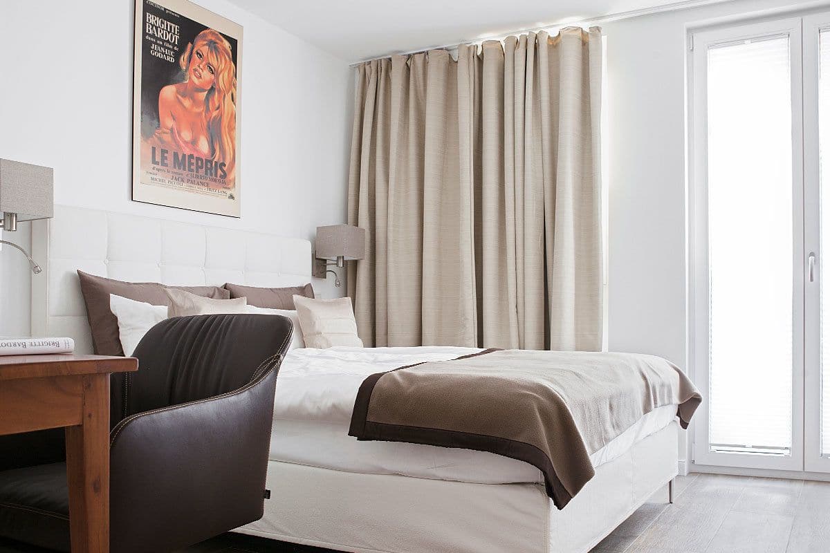A hotel room with a bed, a chair, a desk, a lamp, and a poster on the wall.