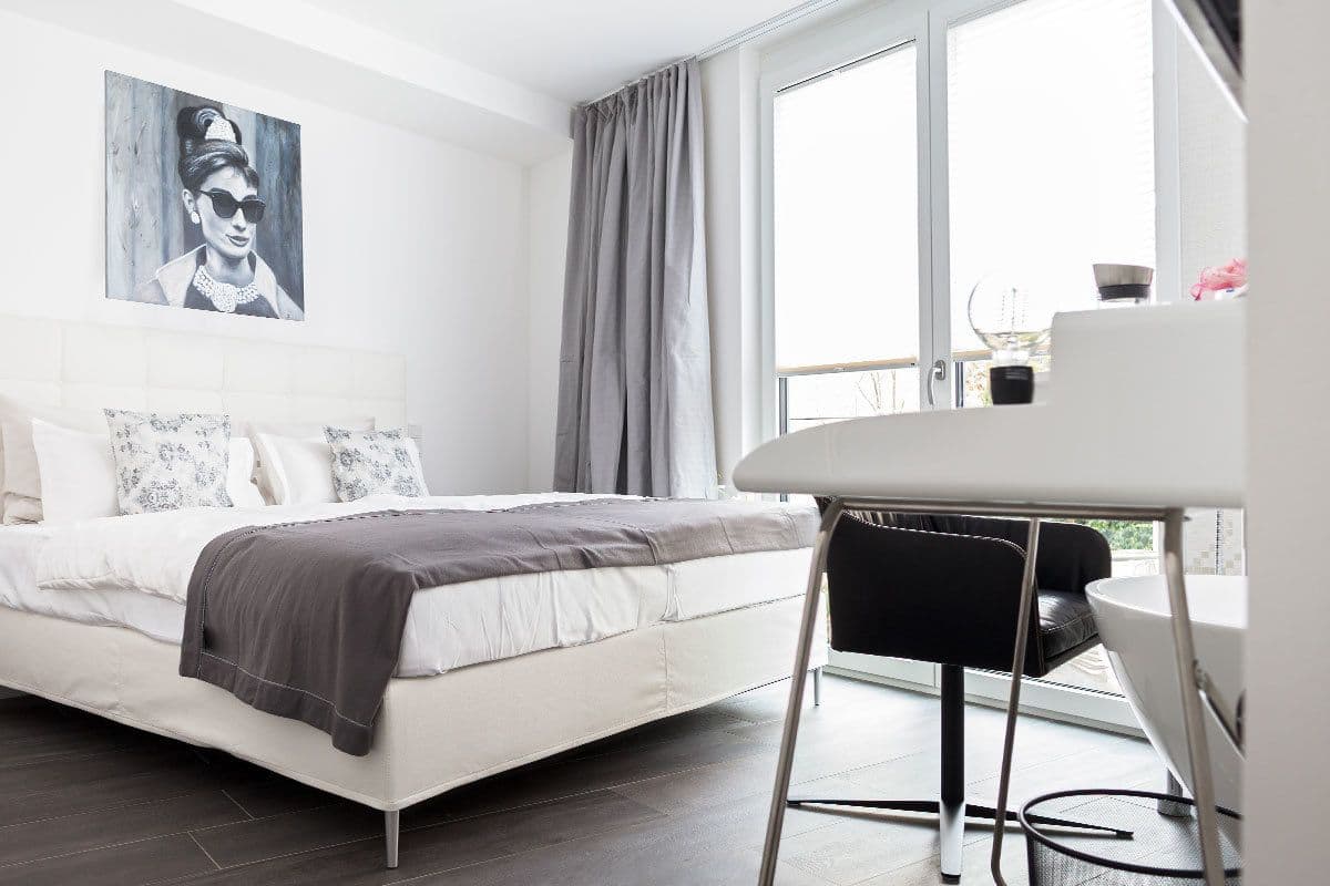 A modern bedroom with a white bed, grey curtains, and a large window.