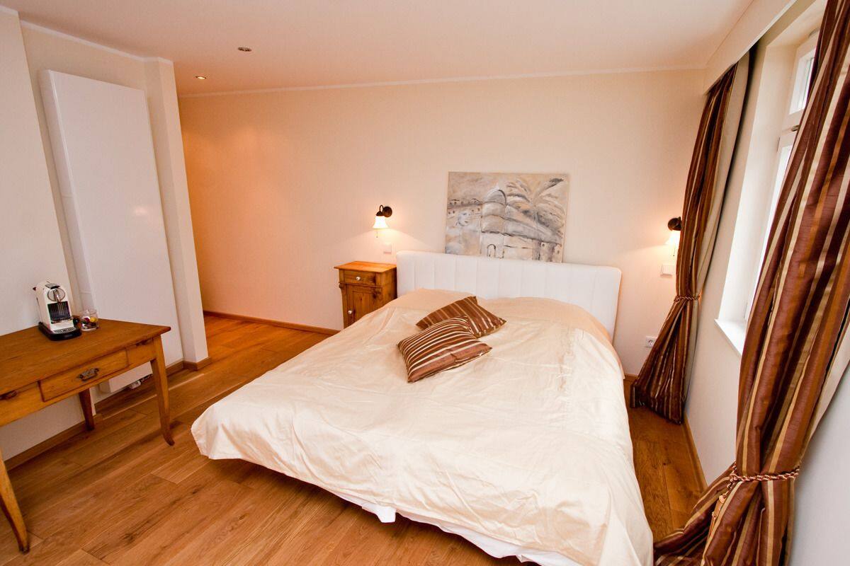 A bedroom with a bed, a bedside table, a lamp, a painting on the wall, and curtains.