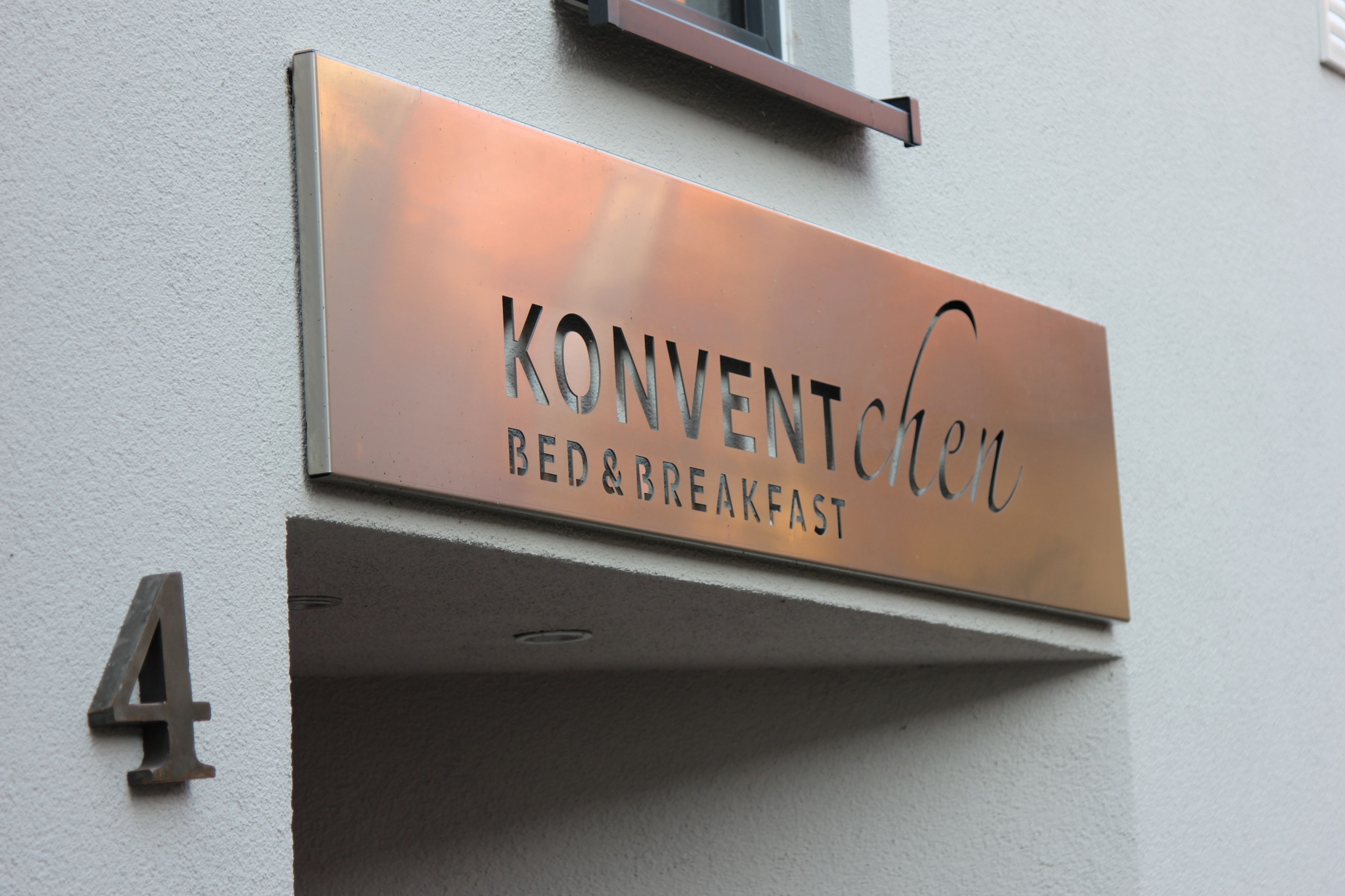 A metal sign with the text "KONVENTICHEN BED & BREAKFAST" mounted on a wall, indicating a bed and breakfast establishment.