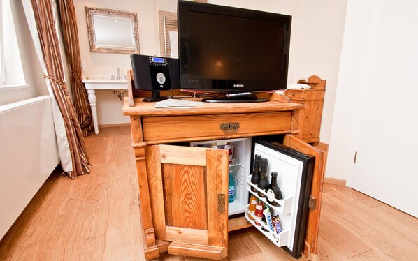 A compact room with a wooden desk, a television, a small refrigerator, and a mirror on the wall. - Konventchen (Aschaffenburg)
