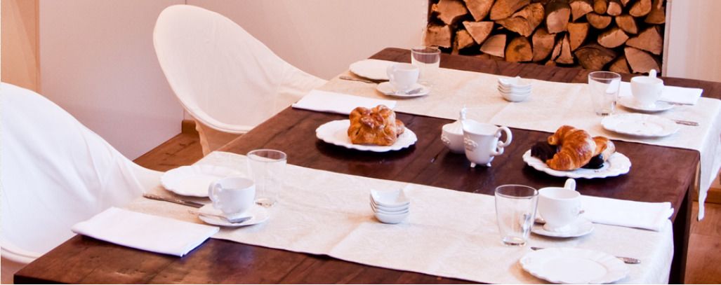 Mesa de comedor dispuesta con vajilla blanca, incluyendo platos, tazas y una tetera, con un rústico fondo de madera.