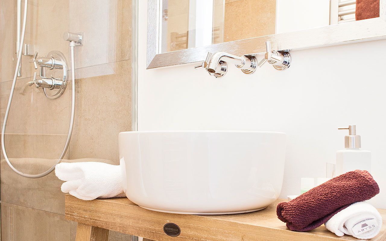Un baño con un lavamanos blanco, un espejo, una ducha y un perchero para toallas.