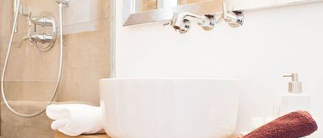 Un baño con un lavamanos blanco, un espejo, una ducha y un perchero para toallas.