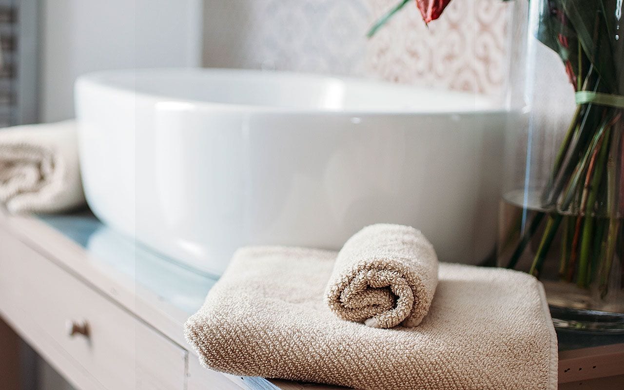 A bathroom with a white sink, a rolled towel, and a vase with flowers.