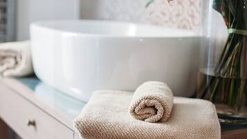 A bathroom with a white sink, a rolled towel, and a vase with flowers.