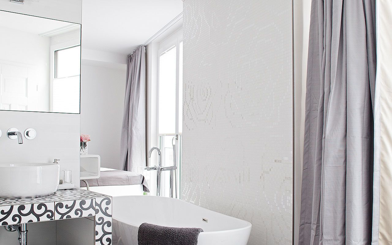 Un baño moderno con una bañera independiente, un espejo grande y un salpicadero de azulejos estampados.