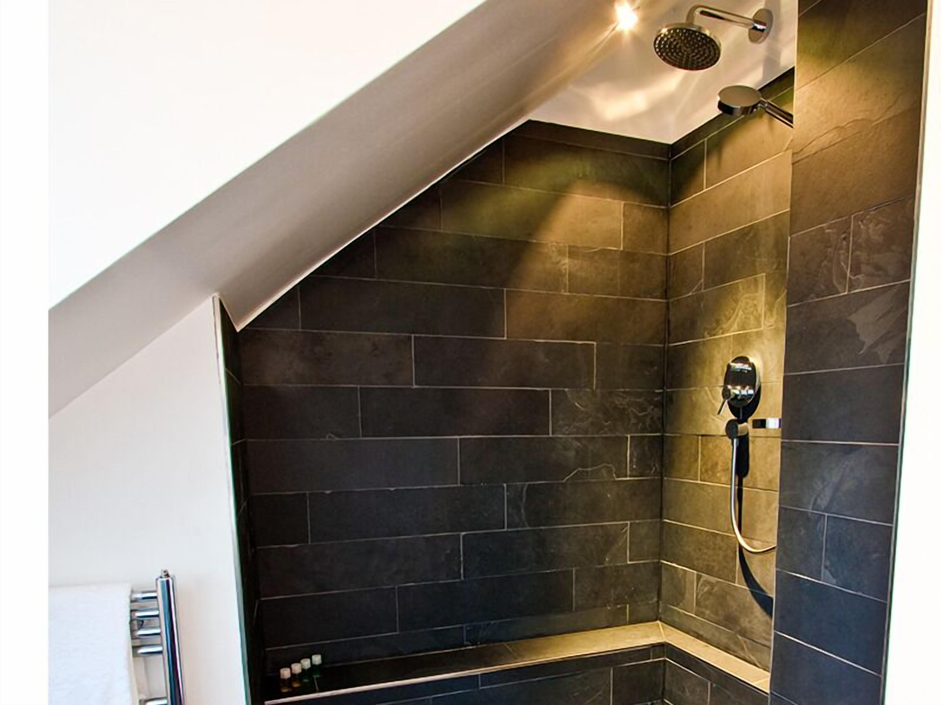 Ducha con azulejos oscuros y cabezal de ducha de mano.