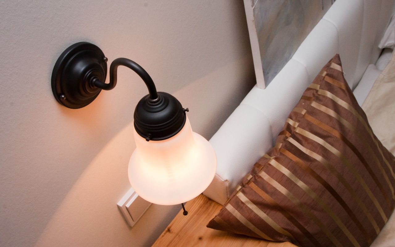 Eine an der Wand befestigte Leuchte mit gebogenem Design und einer kugelförmigen Glaskugel, neben einer weißen Steckdose und einem gestreiften Kissen auf einer Holzoberfläche.