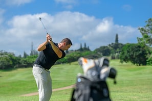 En person på en golfbana med en golfklubba, en golfbag och en klar himmel.