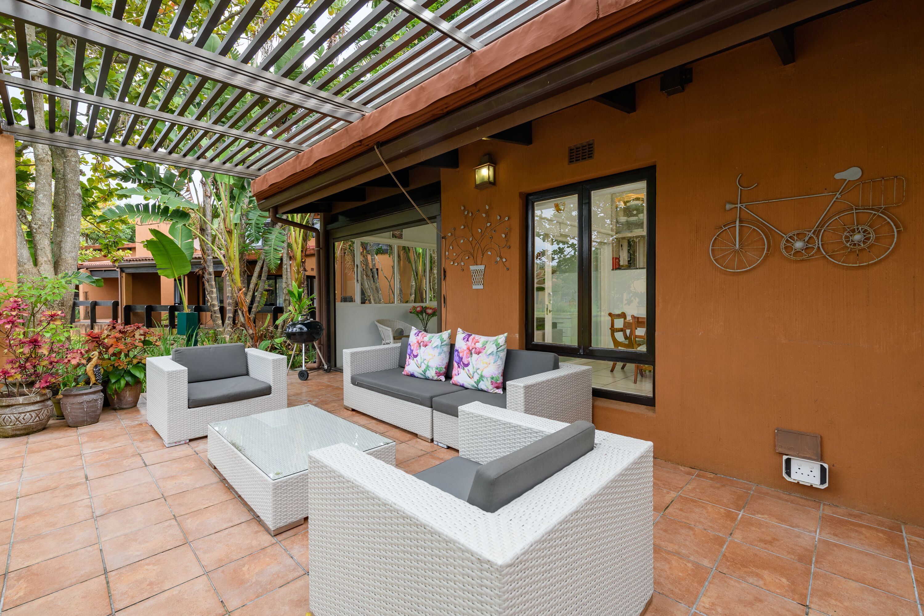 A patio area with wicker furniture, a bicycle decoration, and a view of the house.