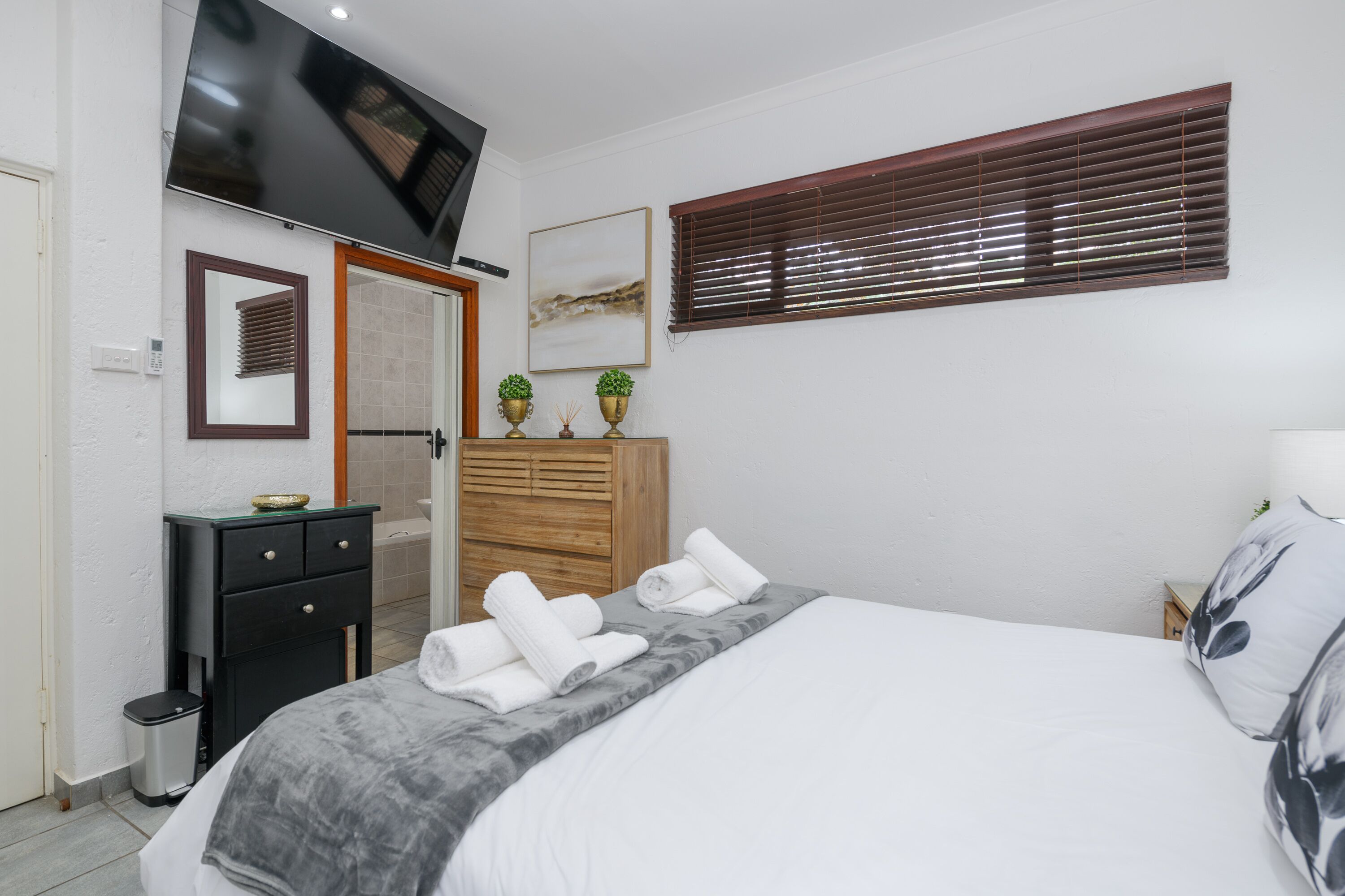 Une chambre bien rangée, avec un lit, une table de chevet et un téléviseur fixé au mur.