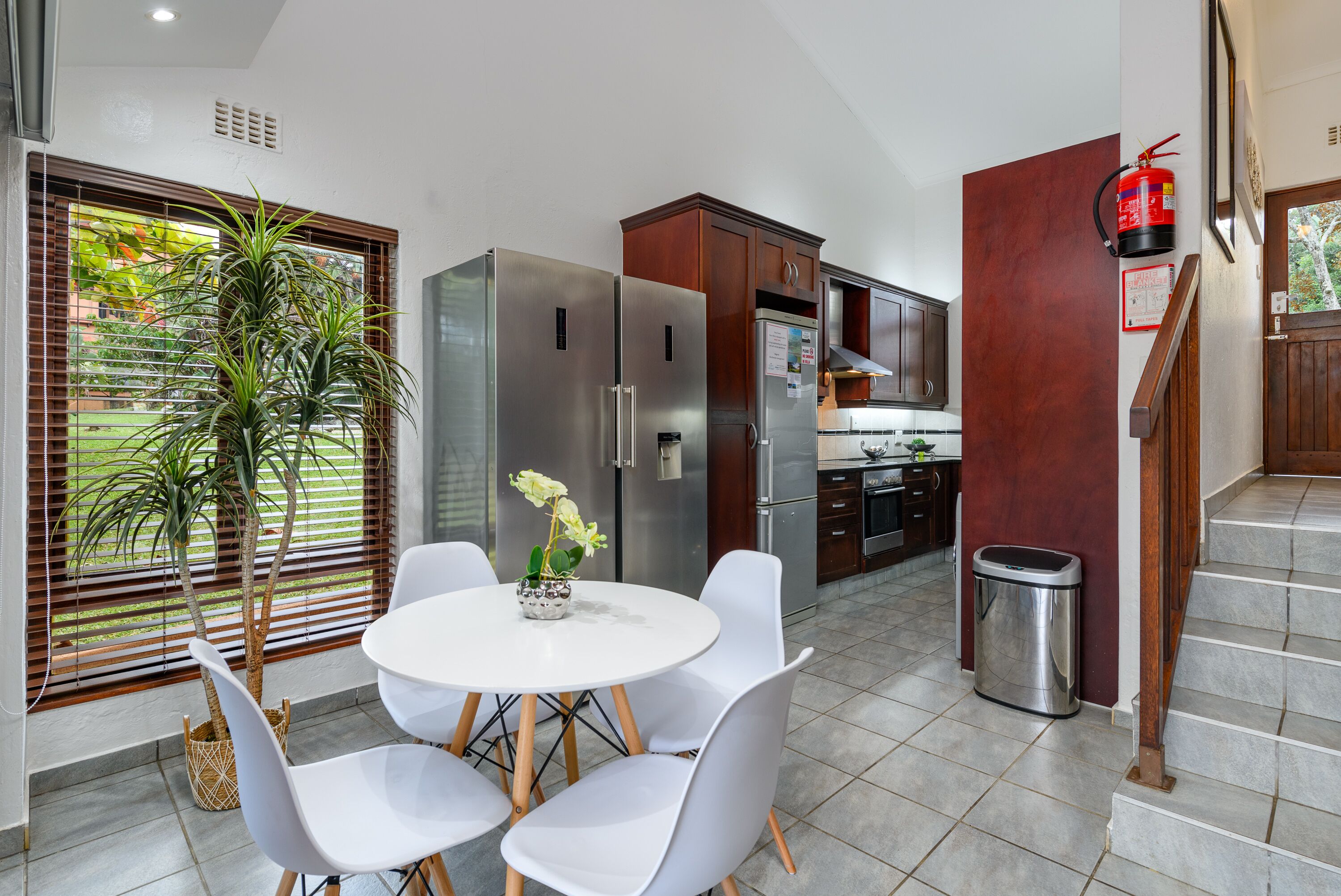 A modern kitchen with stainless steel appliances, a dining area with white chairs, and a staircase.