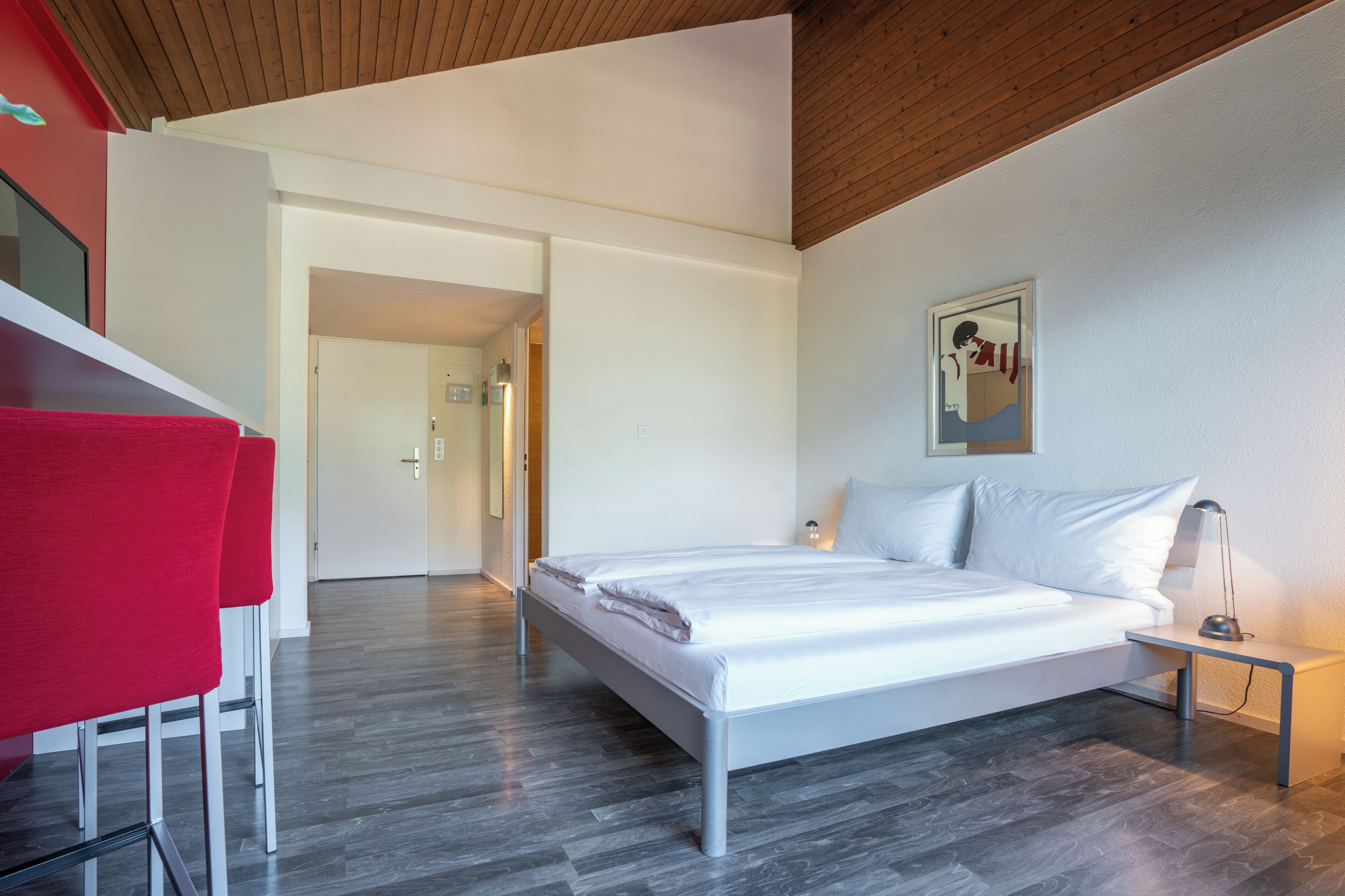 A modern bedroom with a bed, a nightstand, and a red chair.
