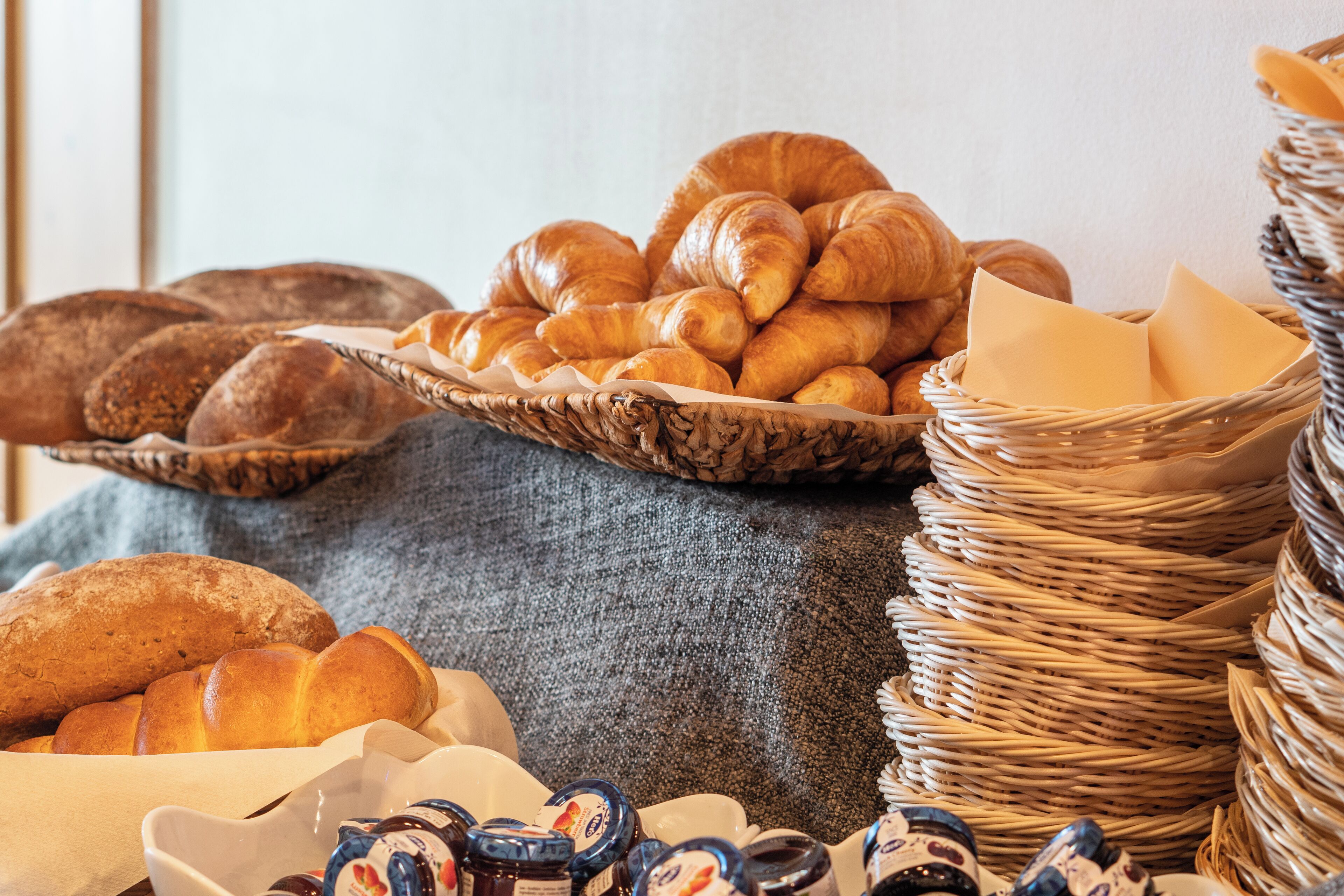 Une variété de viennoiseries et de pains, disposés sur une table avec un panier en osier et un tissu.