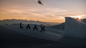 Un snowboardeur effectuant un saut au-dessus d’une pente enneigée, avec le mot « LAAX » visible au premier plan.