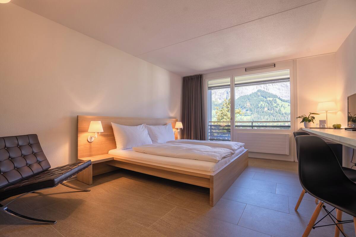 A modern hotel room with a bed, a desk, and a chair.