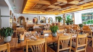Um restaurante com mesas e cadeiras de madeira, plantas em vasos e um teto acolhedor.