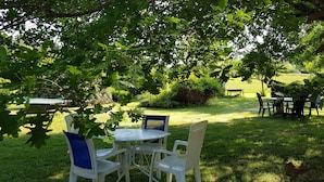 An outdoor seating area with white and blue chairs around a small table, surrounded by lush greenery and trees. - Les Filolies (Saint-Andre-d'Allas)