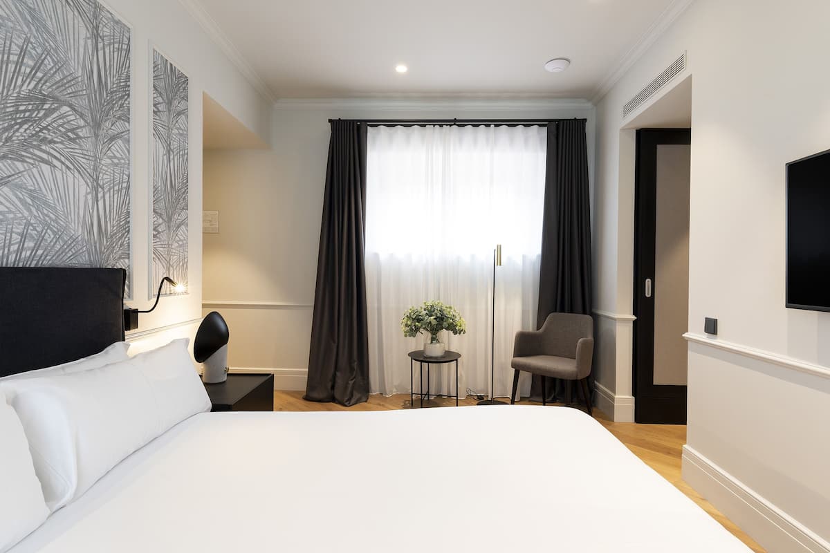 A hotel room with a large bed, a desk with a chair, a small table with a plant, and a TV on the wall.