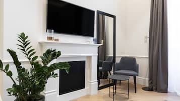 Ein modernes Wohnzimmer mit einem Flachbildfernseher über einem weißen Kamin, einer Topfpflanze, einem grauen Sessel und einem kleinen runden Tisch.