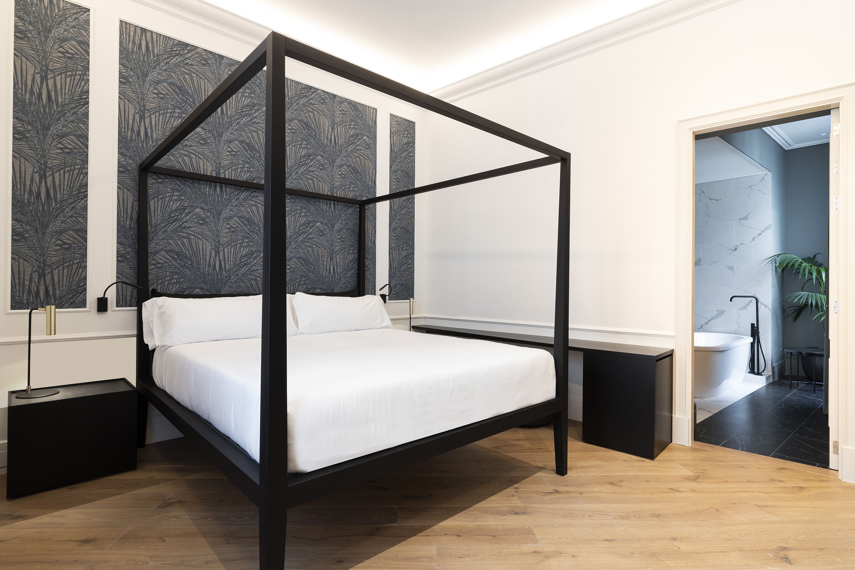 Ein modernes Schlafzimmer mit einem Himmelbett, einem Nachttisch, einem Beistelltisch und Blick auf ein Badezimmer durch eine offene Tür.
