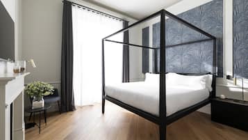 A modern bedroom with a four-poster bed, a small desk with a chair, a vase of flowers, and a large window with curtains.