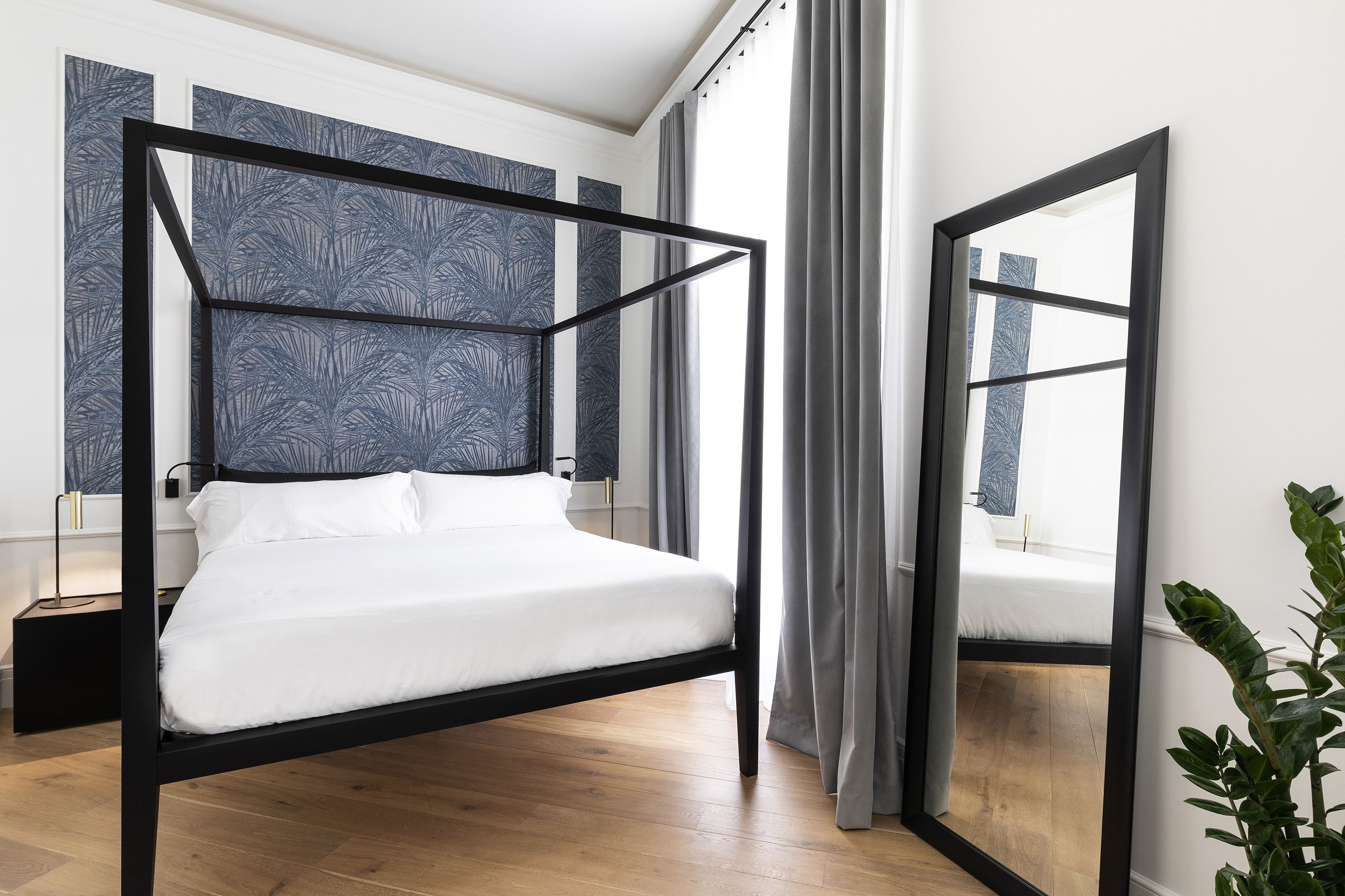 Un dormitorio moderno con estructura de cama de metal negro, ropa de cama blanca y un amplio ventanal con cortinas.