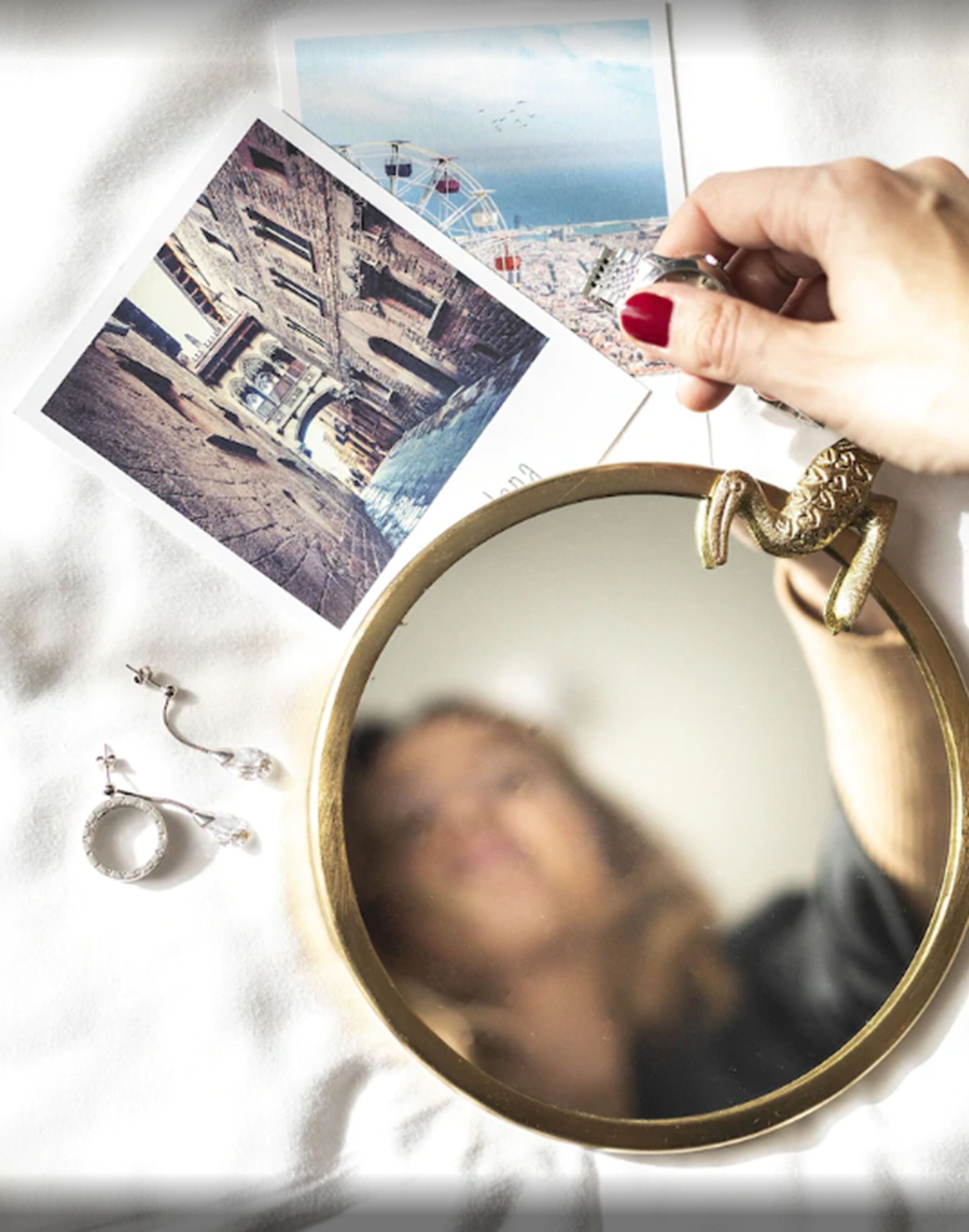 A hand holding a key, a round mirror, and a photograph of a cityscape with a bridge.
