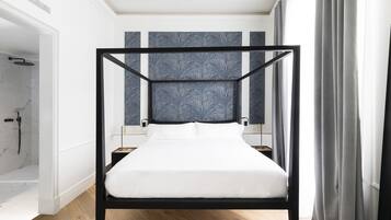 A modern bedroom with a four-poster bed, a marble shower, and a view of the city.