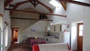 A spacious living area with a red sofa, a kitchen with white cabinets, and a staircase leading to an upper level. - Gîtes de la Ferme du Luc (Braslou)