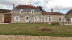 A two-story building with a tiled roof, a gravel driveway, and a grassy lawn. - Gîtes de la Ferme du Luc (Braslou)