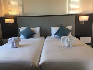 A hotel room with two beds, each with white linens and pillows, and a headboard. There are wall-mounted lamps on either side of the bed. - La Playa Beach Front Pool Villa Cha-am (Cha-am)