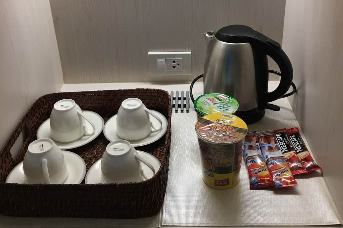 A kitchen area with a kettle, a basket of cups, a container of cereal, and packets of coffee.