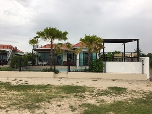 A modern house with a swimming pool, surrounded by palm trees and a sandy area. - La Playa Beach Front Pool Villa Cha-am (Cha-am)