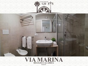 Un baño moderno con un lavabo grande, cabina de ducha con mampara de cristal y un espejo sobre el lavabo.