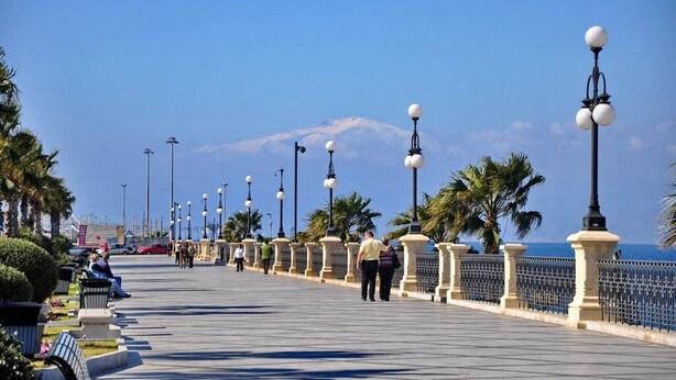 Une promenade offrant une vue dégagée sur une montagne au loin, bordée de lampadaires et de palmiers.