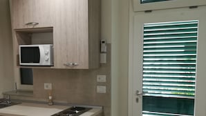 Una cocina moderna con armarios de madera, microondas integrado y una puerta de vidrio con persianas.