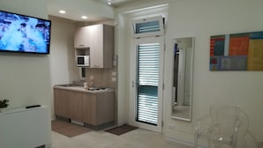 Una cocina moderna con microondas integrado, un lavamanos pequeño y una encimera. Hay un televisor en la pared mostrando un evento deportivo.
